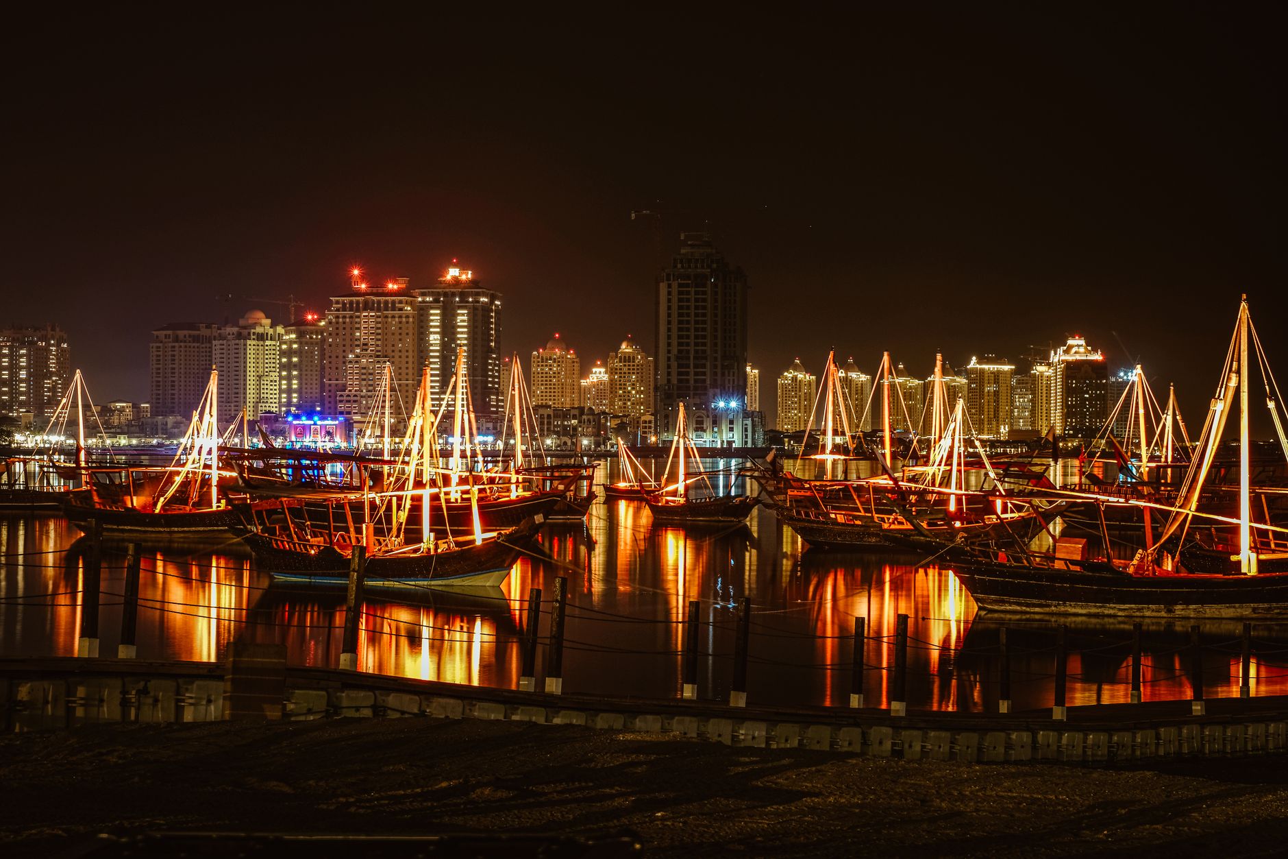Beeindruckende Ansicht eines Stadt Hafens bei Nacht, mit beleuchteten Segelbooten und Wolkenkratzern, die sich im ruhigen Wasser spiegeln.