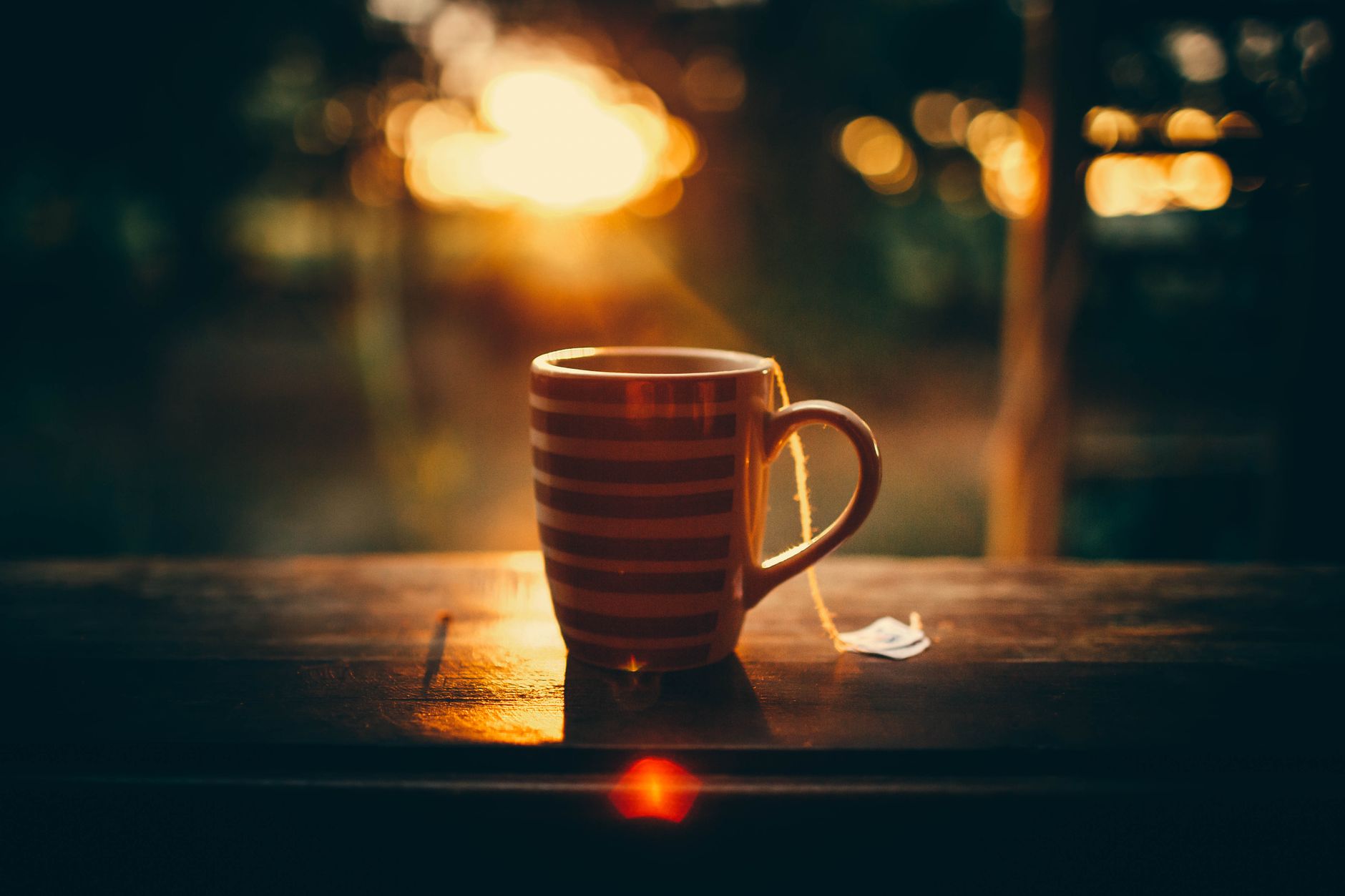 Eine gemütliche gestreifte Teetasse auf einem Holztisch im Freien mit warmem Glanz der Sonne beim Untergang.