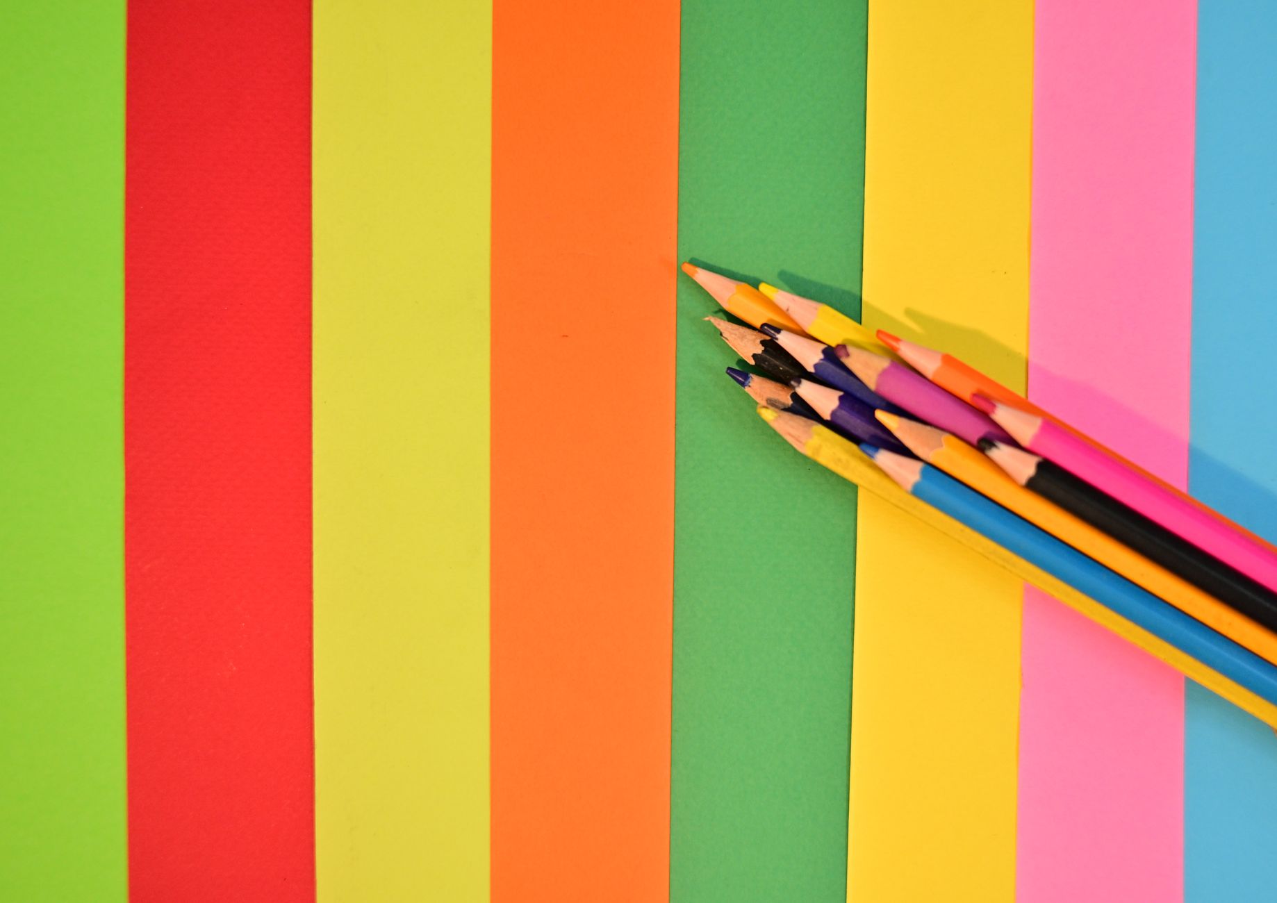 Leuchtend bunte Stifte auf einem farbenfrohen, gestreiften Papierhintergrund – ein Beweis für die Kreativität.