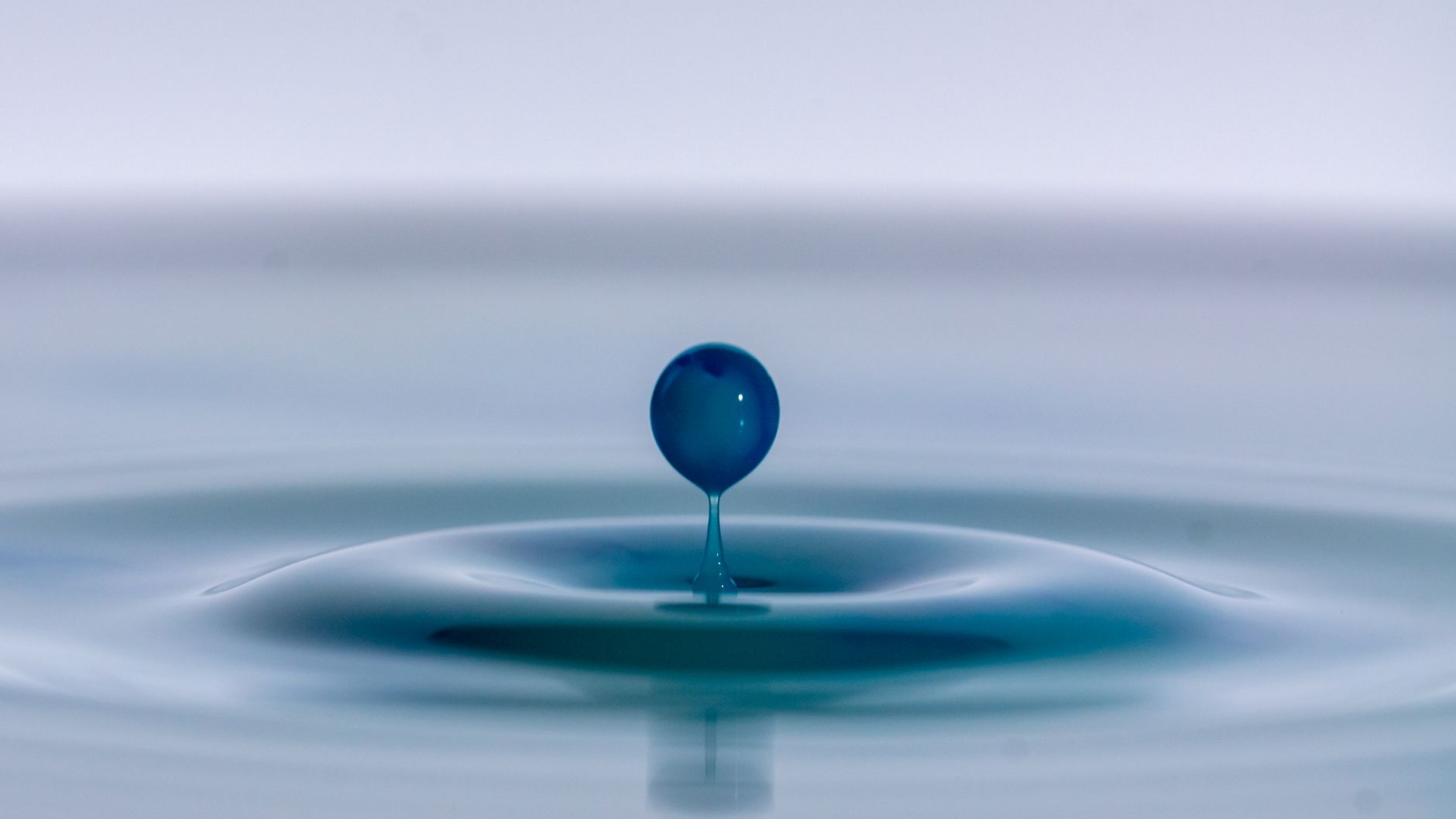 Nahaufnahme-Makrofotografie, die einen einzelnen blauen Wassertropfen festhält, der Wellen erzeugt.