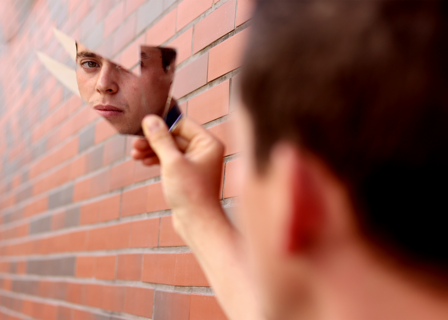 Das Gesicht eines Mannes wird in einem Fragment eines Spiegels widergespiegelt, das gegen eine Ziegelwand gehalten wird.