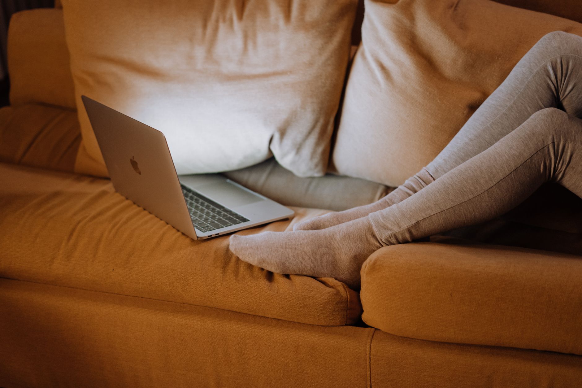 Bequeme Büroeinrichtung zu Hause mit Beinen auf einem Sofa, das einen Laptop für die Arbeit verwendet.
