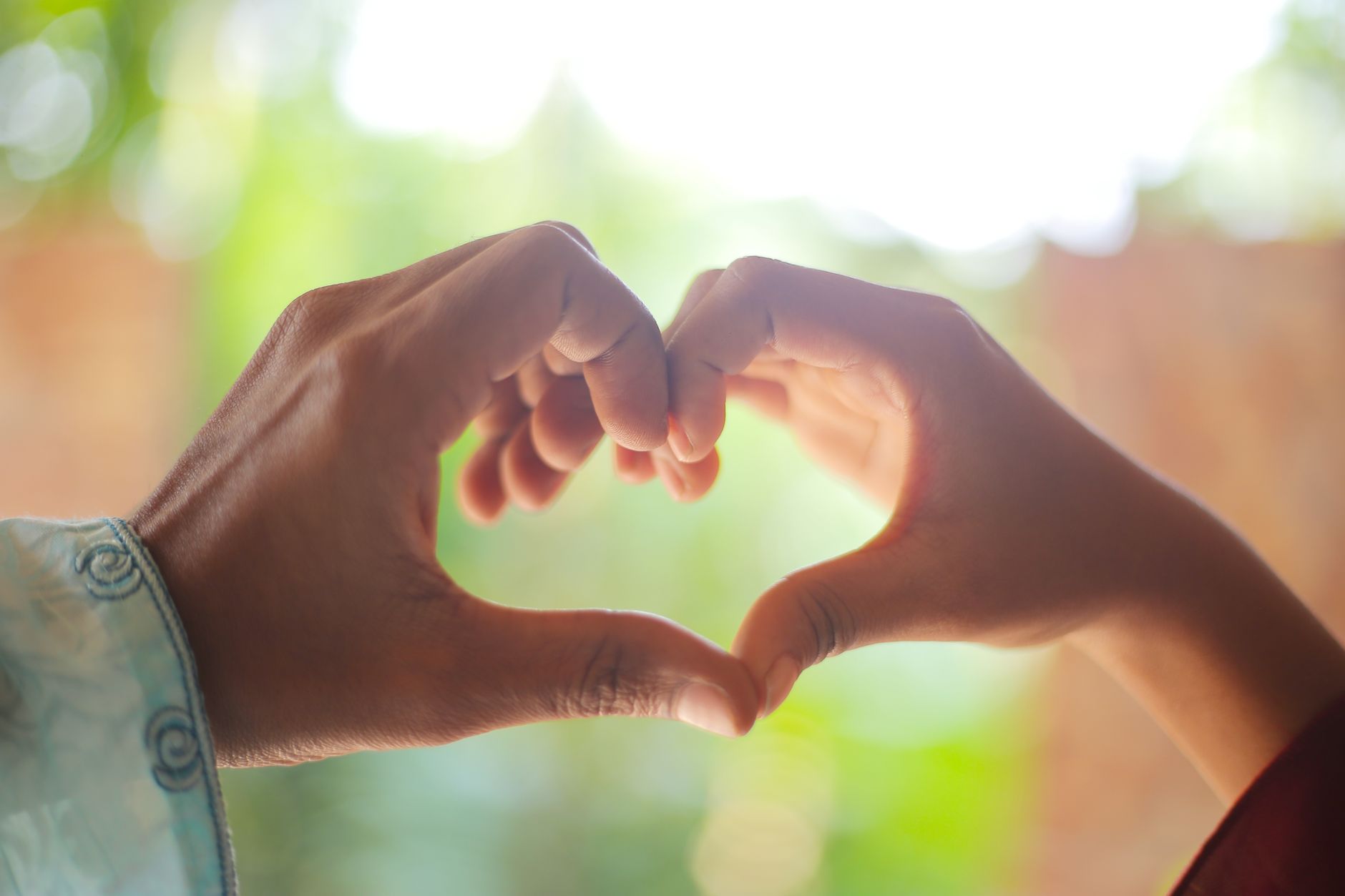 Eine Nahaufnahme von zwei Händen, die im Freien eine Herzform bilden, symbolisiert Liebe und Verbindung.