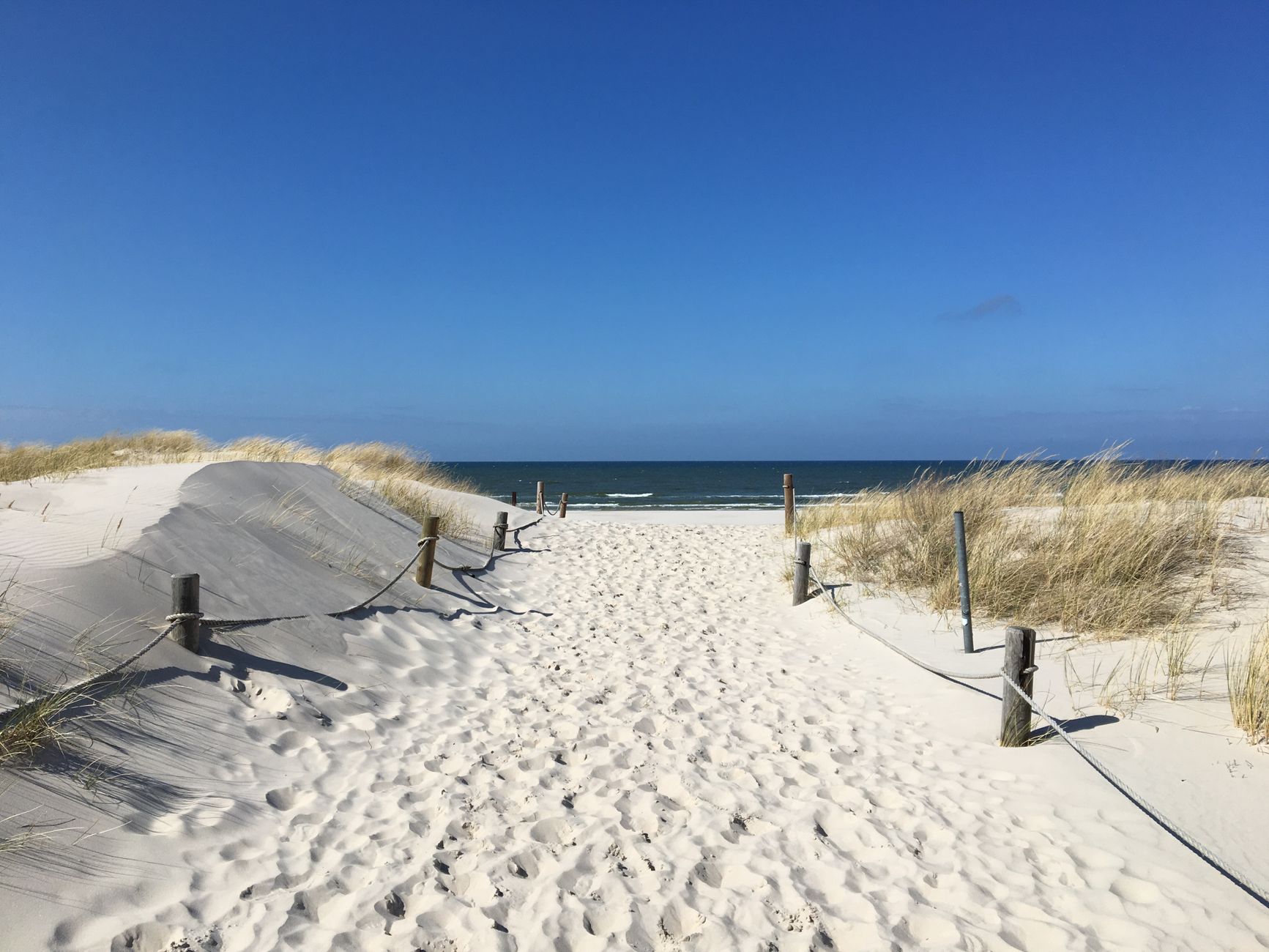 Malerscher Sandweg, der zum Strand führt, mit klarem blauen Himmel in Łeba, Polen.