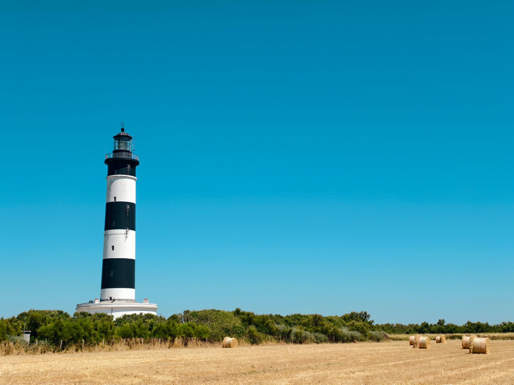 Faszinierender Blick auf den Leuchtturm von Chassiron mit Heuballen unter einem klaren blauen Himmel in Saint-Denis-d'Oléron.