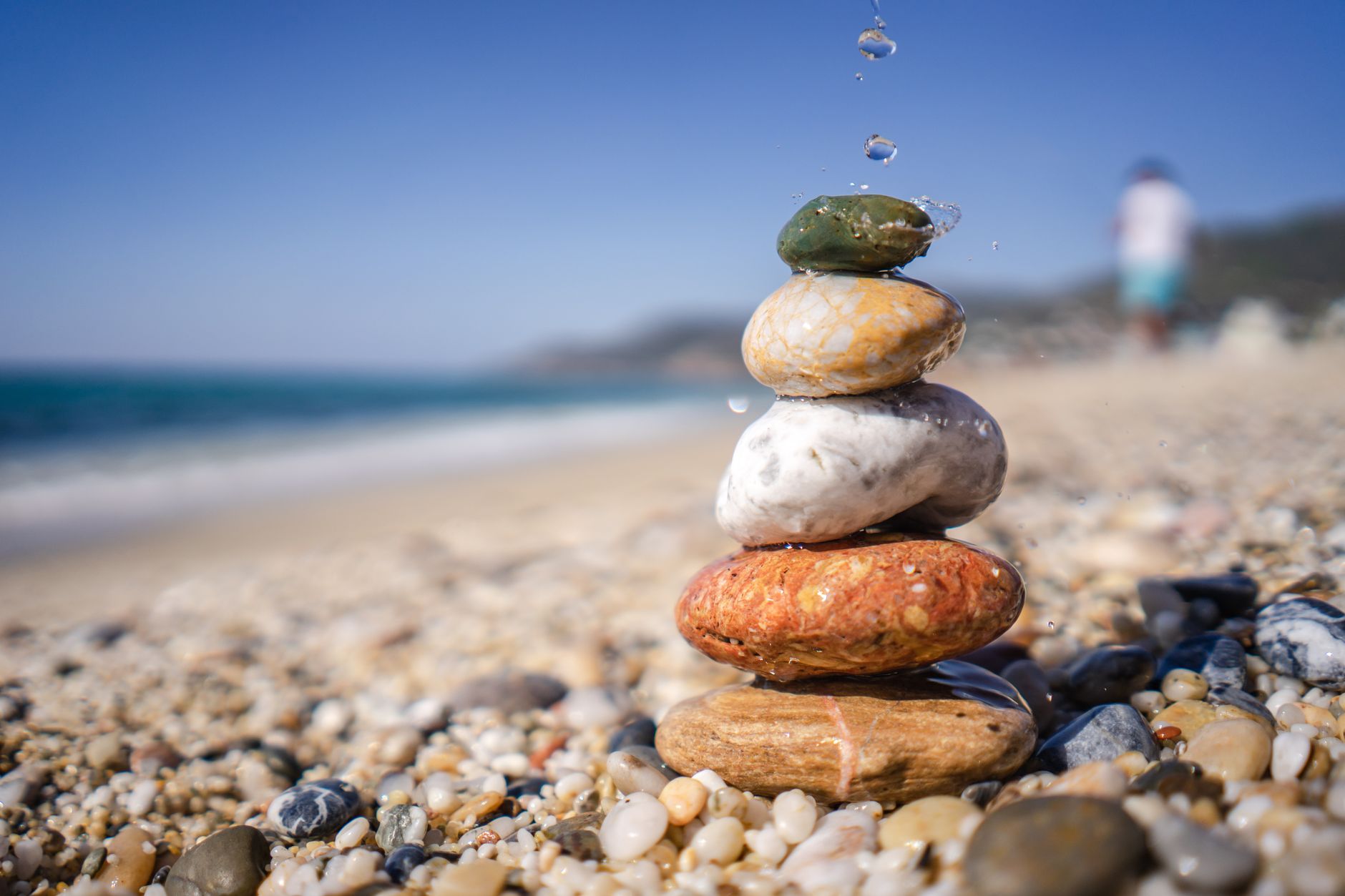 Nahaufnahme von gestapelten Steinen, die an einem ruhigen Kiesstrand balancieren und Zen sowie Stabilität symbolisieren.