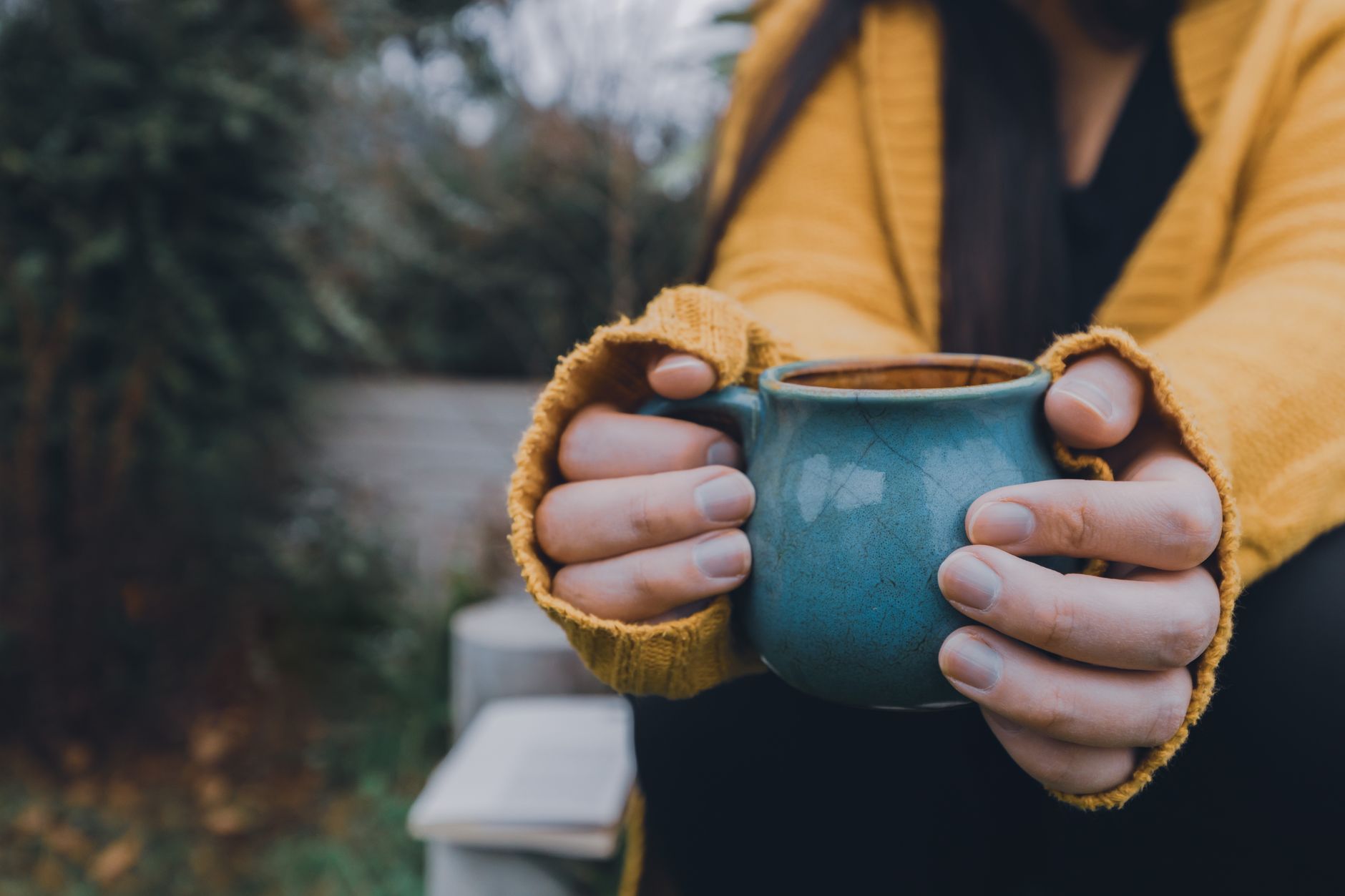 Hände halten eine blaue Tasse in einem warmen Pullover im Freien und fangen eine gemütliche Herbststimmung ein.