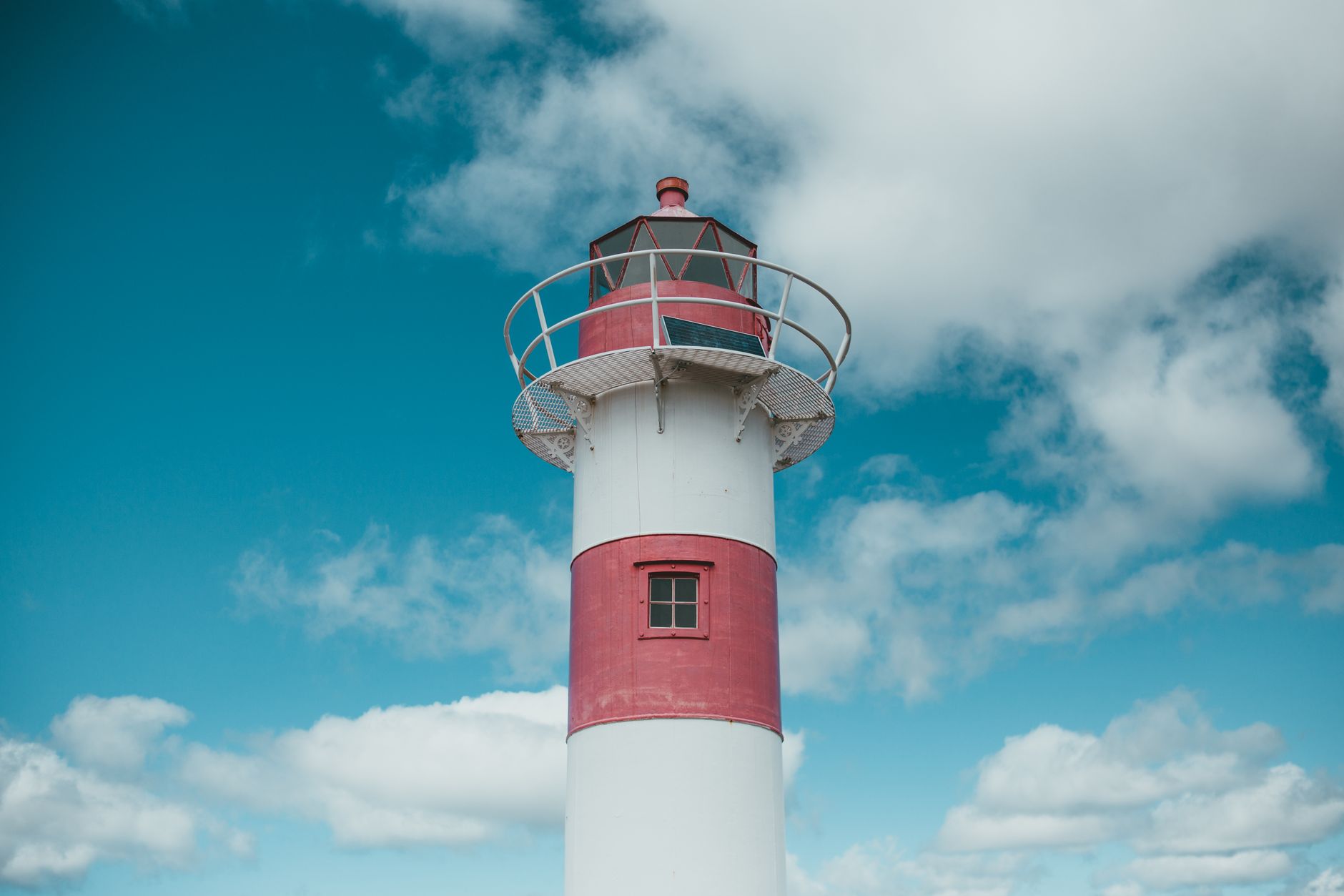 Ein lebhafter roter und weißer Leuchtturm erhebt sich vor dem Hintergrund eines klaren blauen Himmels und verstreuter Wolken.